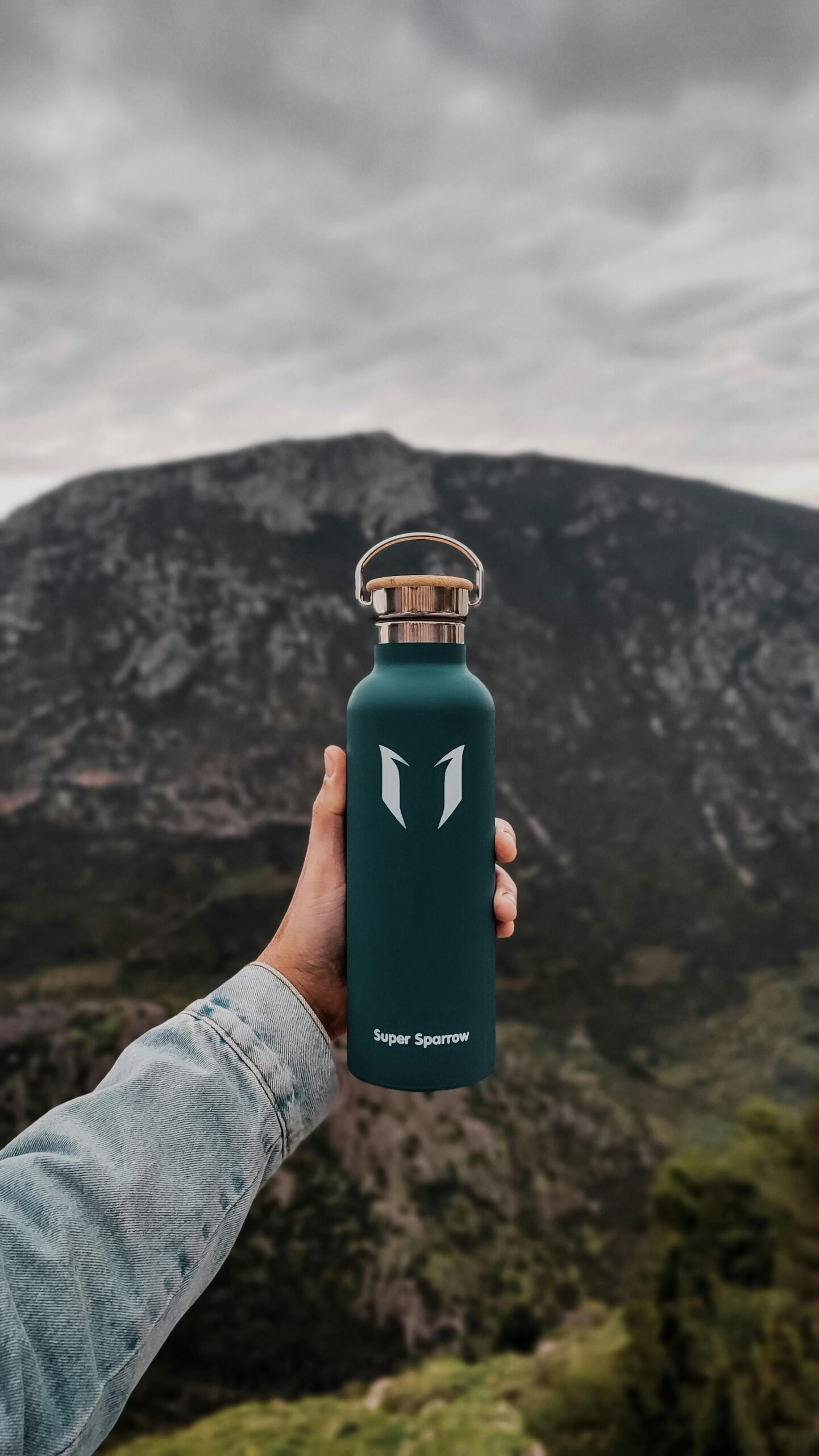 A hand holds a reusable water bottle with a scenic mountain view in Delphi, Greece.